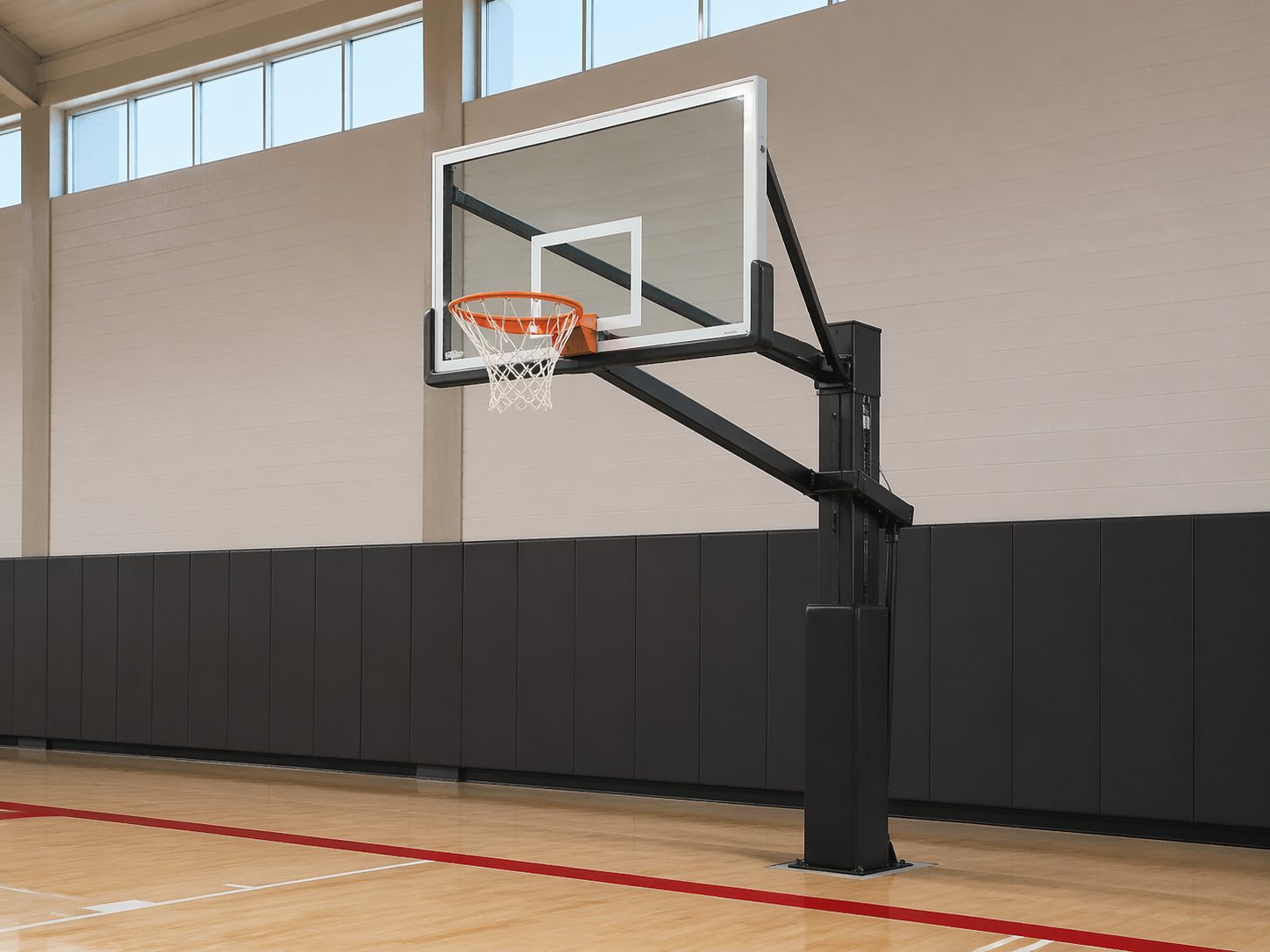In-ground adjustable basketball goal against clean gymnasium wall with glass backboard, ProHeavyFitness