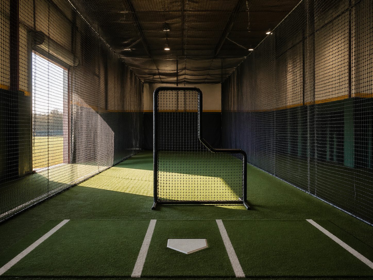 Interior view of netted batting cage tunnel with turf flooring and L-screen in fieldhouse, ProHeavyFitness