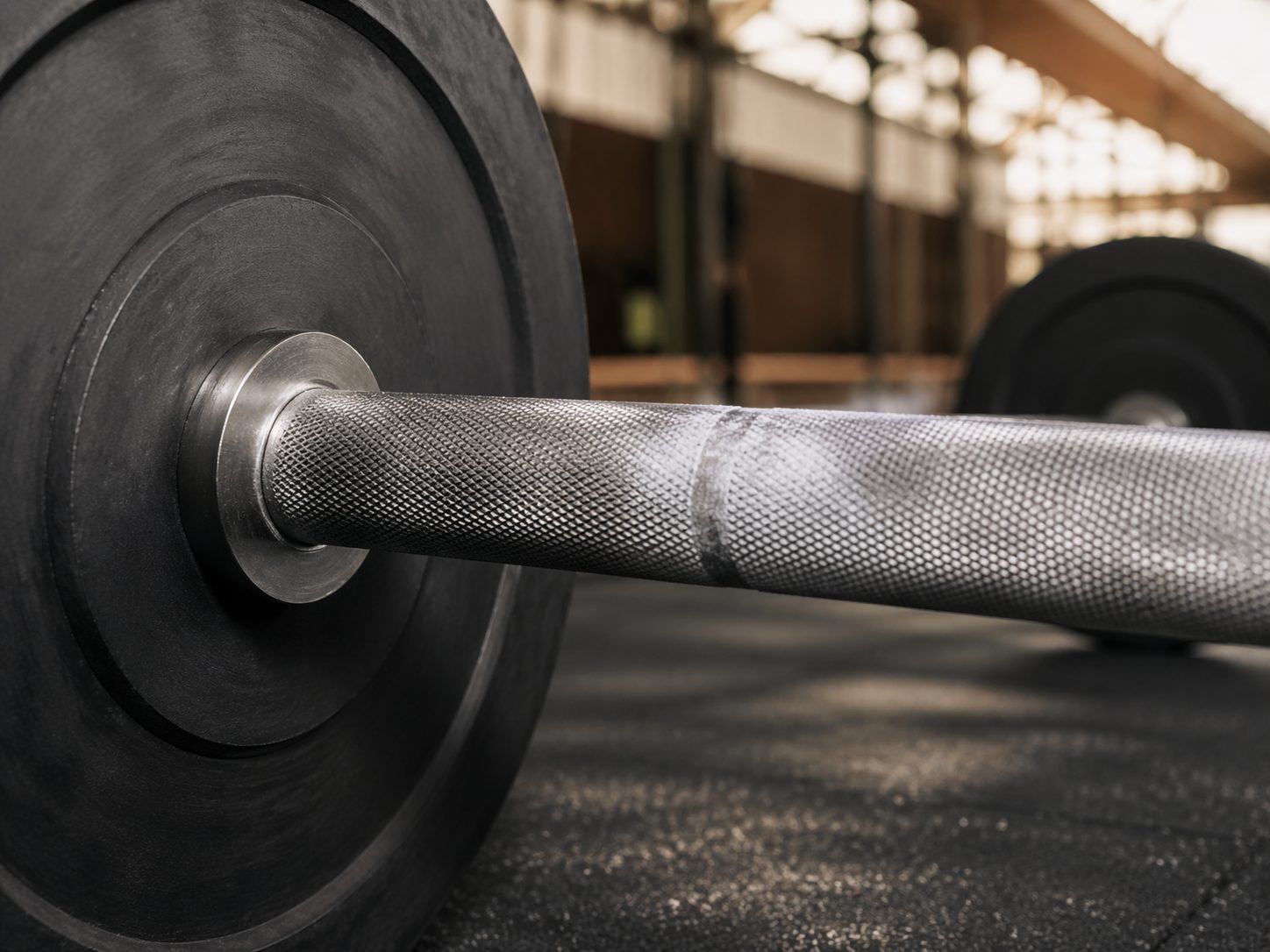 Close-up of knurled Olympic 20kg barbell with chalk dust and matte black bumper plates in Indianapolis weight room, ProHeavyFitness